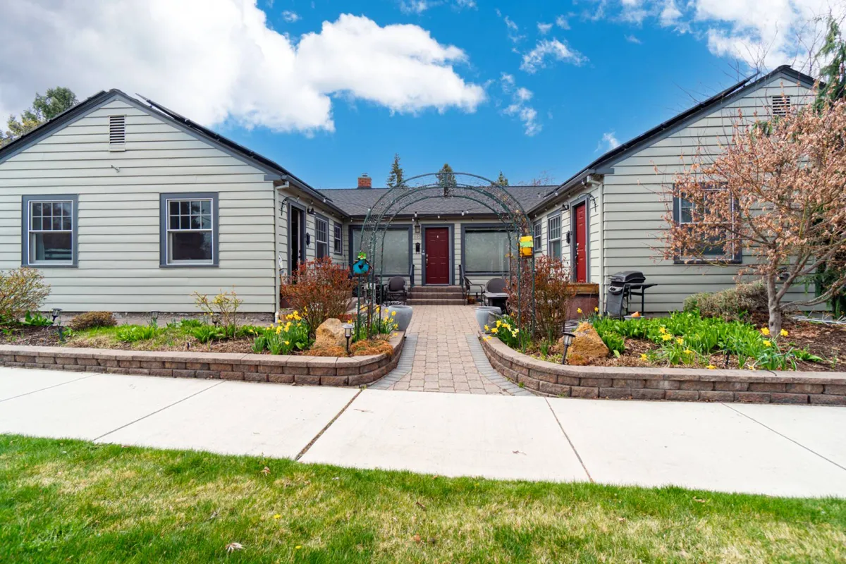The image captures the inviting front entrance of Drake Cottage, framed by an arched walkway and surrounded by lush garden greenery. The scene suggests the ease of stepping outside and immersing yourself in the vibrant neighborhood, with hints of activity like morning coffee or gathering with friends under the archway.