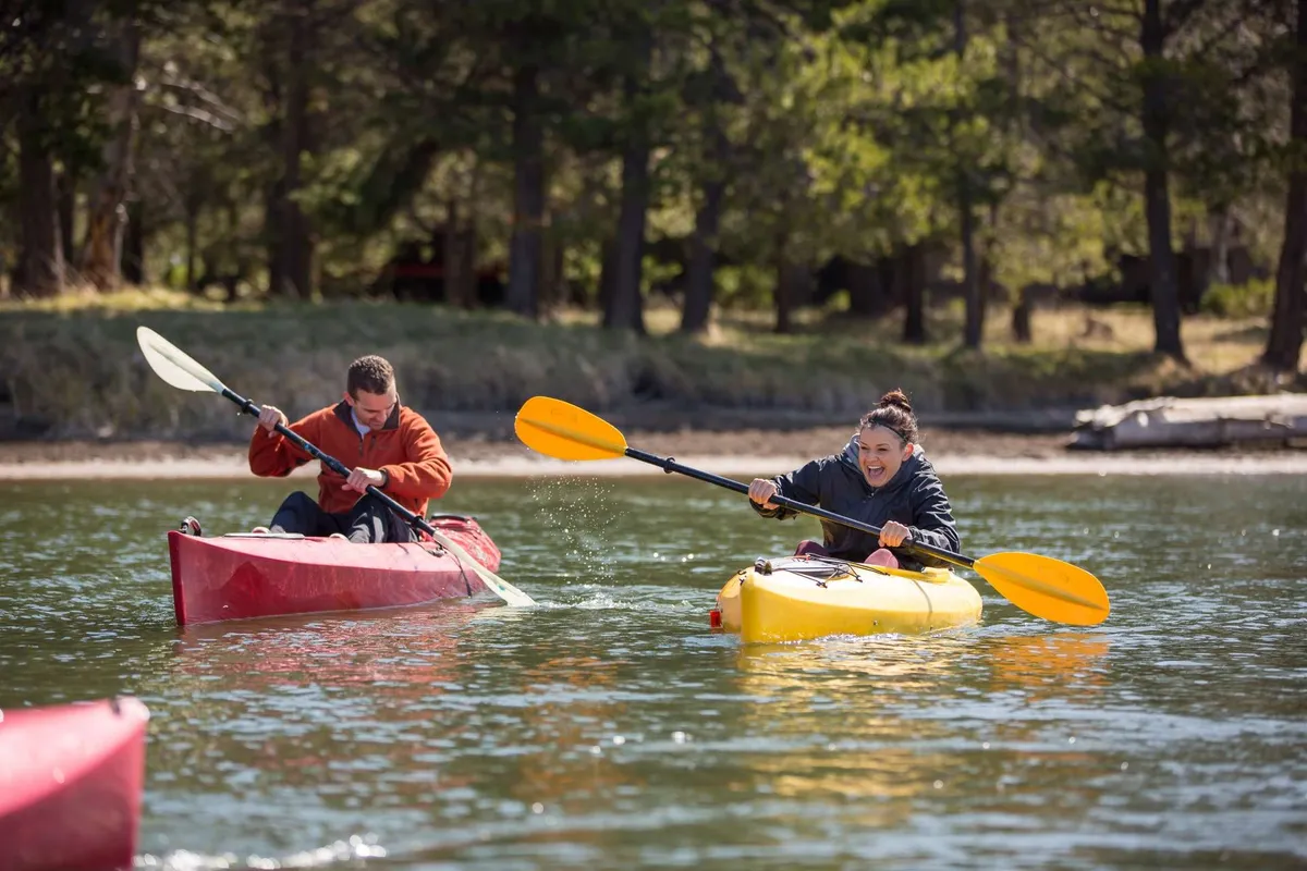 Two people kayak on vibrant yellow and red kayaks over a shimmering river, demonstrating active engagement with local waterways and highlighting opportunities for solo or group adventures in nature.