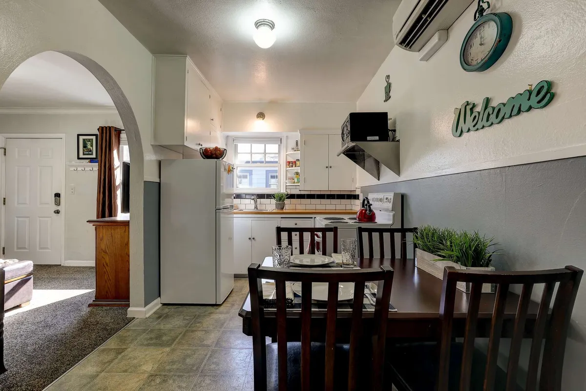 A cozy dining table set near the kitchen, surrounded by kitchen appliances and decorative wall art. A window provides ample natural light, creating a warm and welcoming space for meals and social gatherings.