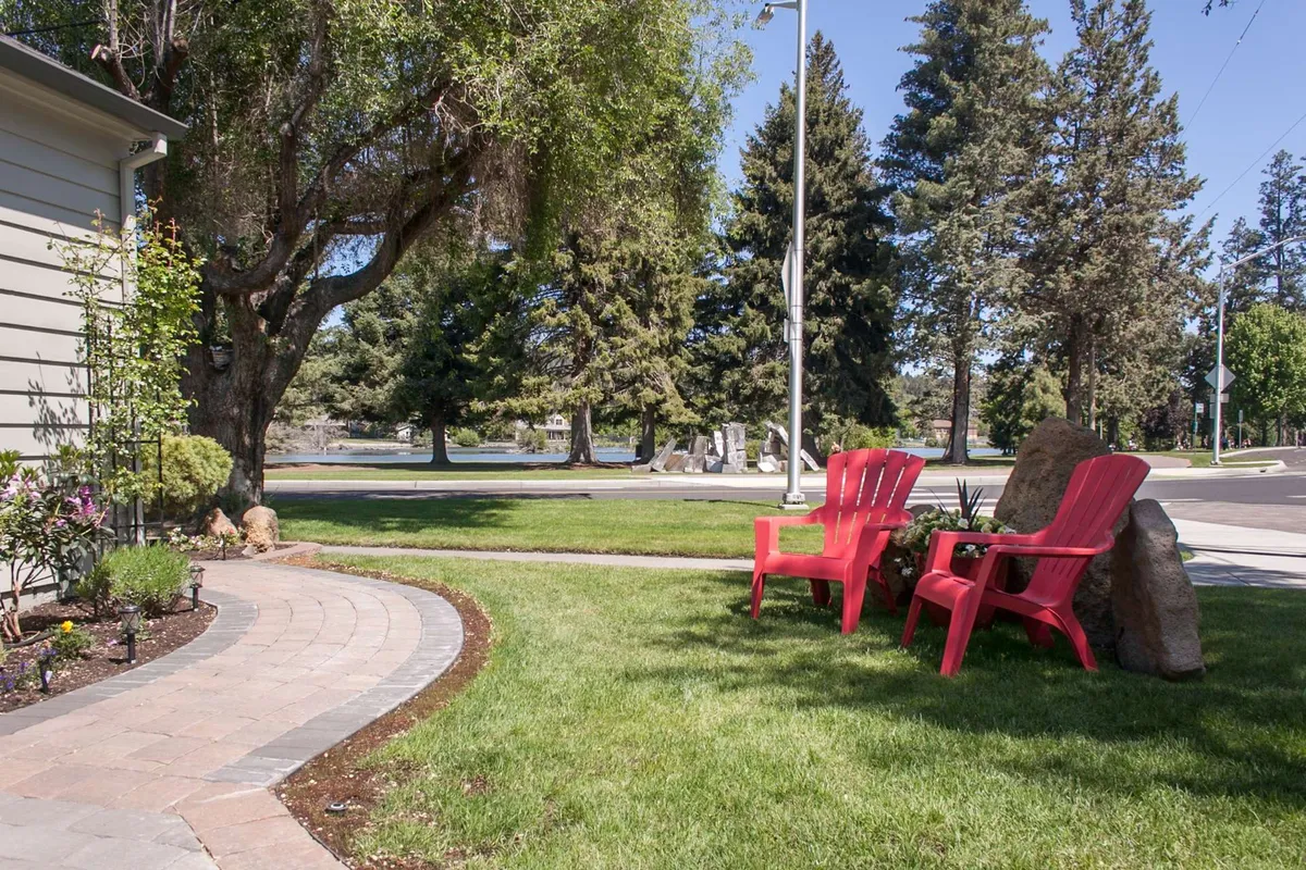 Red chairs face each other along a stone pathway surrounded by lush greenery, creating a welcoming outdoor space that feels both private and connected to nature.