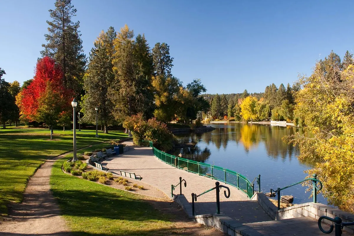 A serene park-like setting with a placid lake, lush trees, winding pathway, and a welcoming seating area. The scene is ideal for picnicking, people-watching, or simply soaking up the vibrant yet tranquil atmosphere central to the section's narrative.