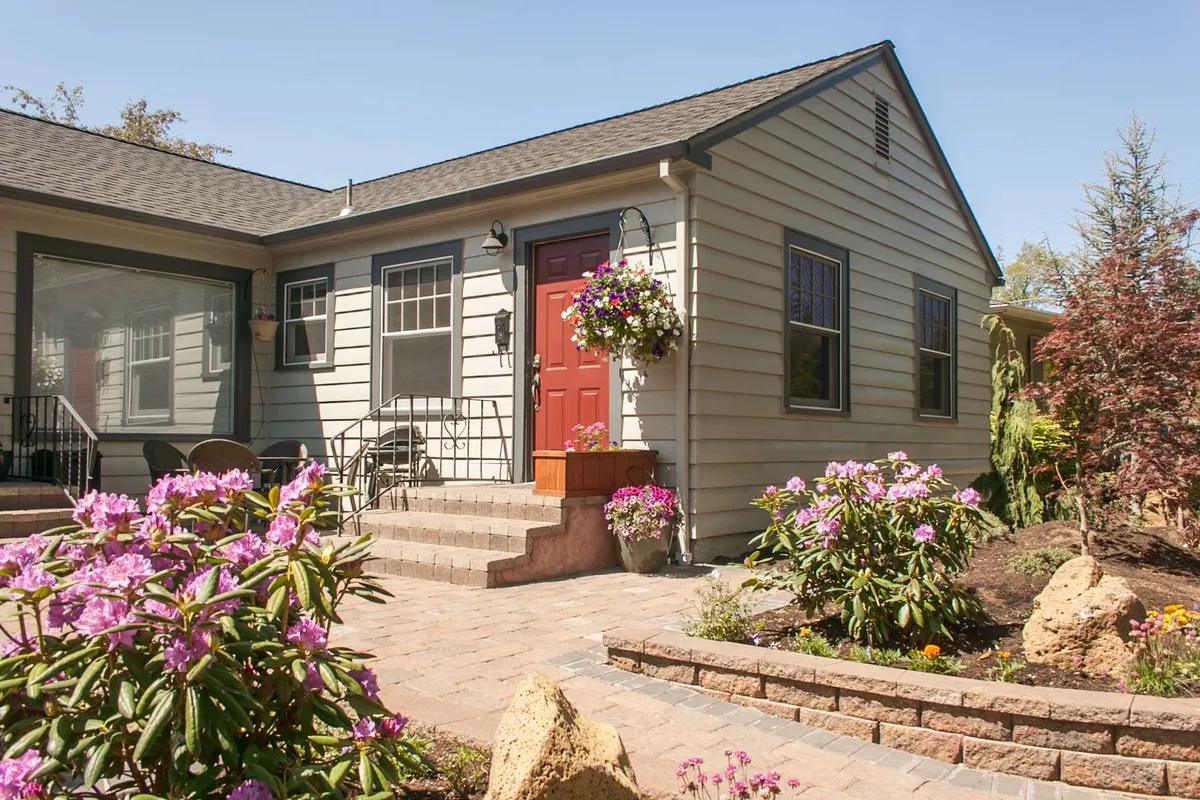 A vibrant exterior shot featuring a bold red front door, flowering plants, and a stone pathway leading to the entrance. The scene radiates warmth and friendliness, hinting at a home that serves as the perfect base for urban adventures and welcoming guests.