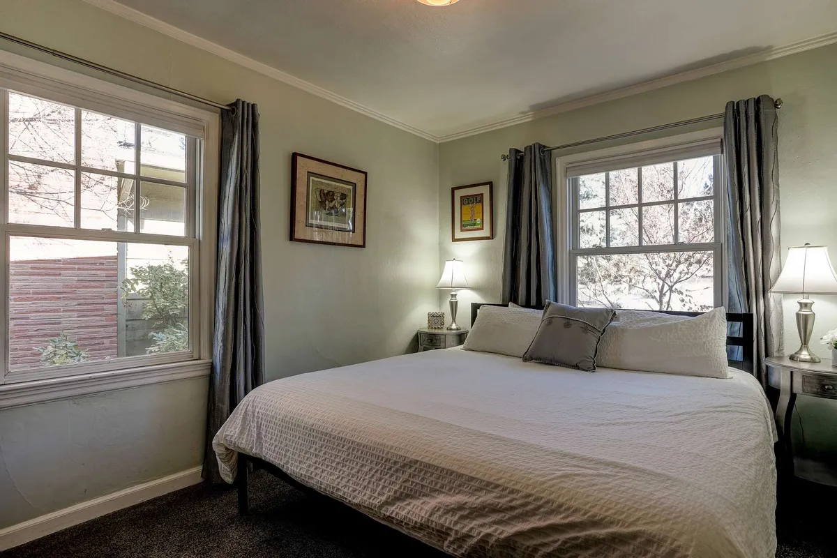 A peaceful bedroom scene featuring a plush queen bed, soft linens, warm nightstands, and framed artwork. Gentle natural light filters through the windows, creating an inviting and restful atmosphere ideal for unwinding.